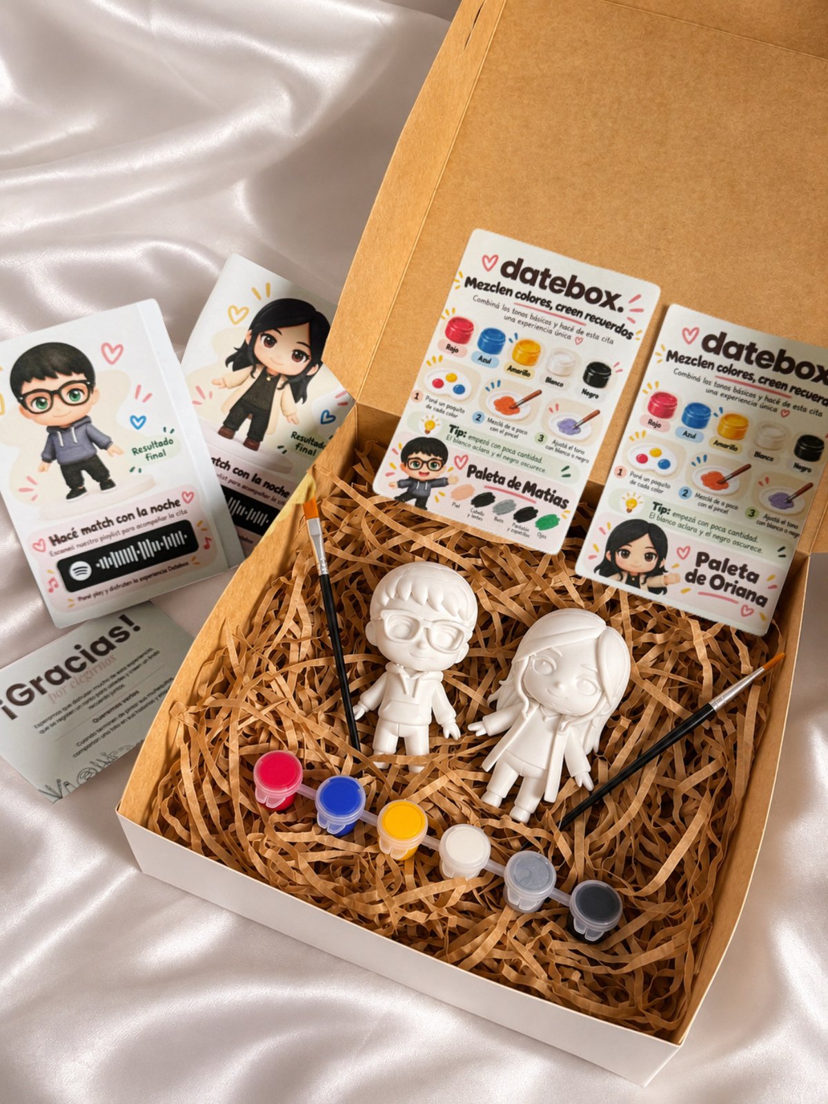 Caja abierta de Datebox con figuras personalizadas de una pareja, pinturas, pinceles y guías de colores